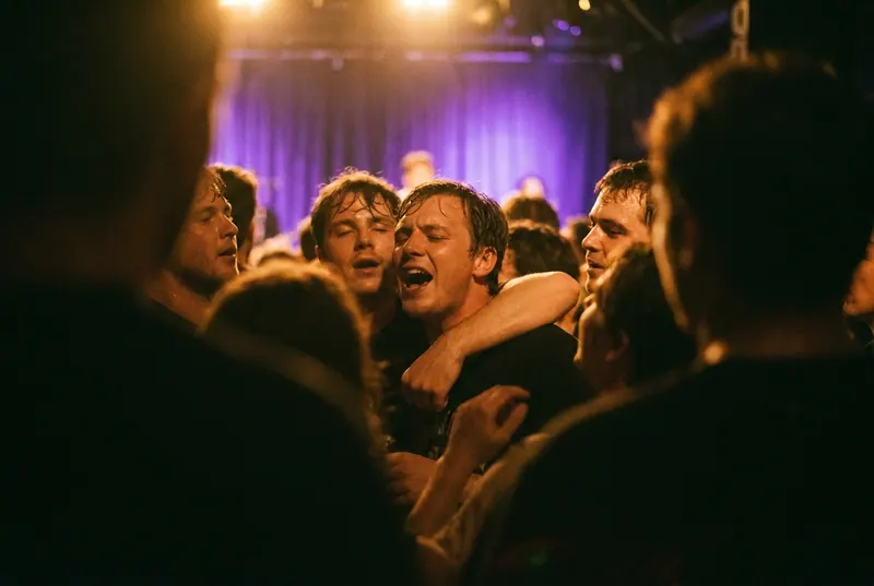 A small crowd at a gig, faces lit from the stage, one person singing along