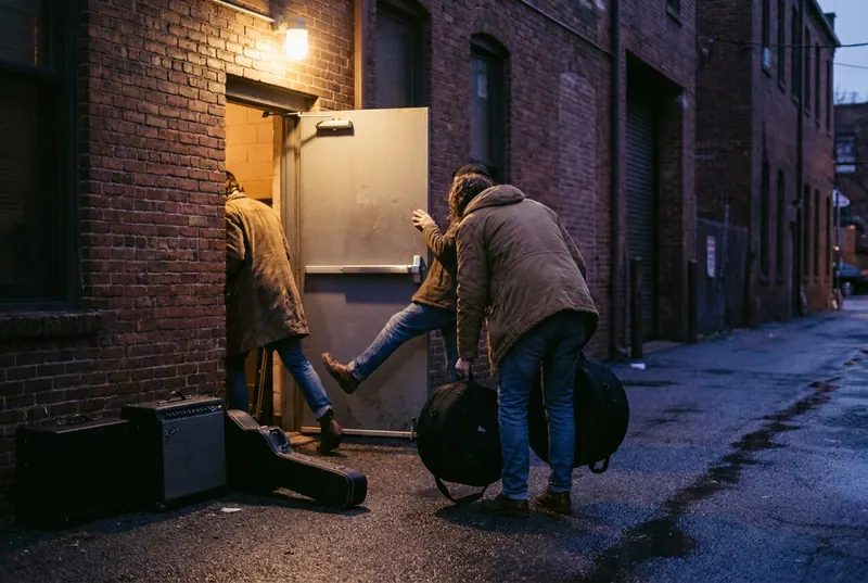 A band loading gear in through a venue's back door at dusk