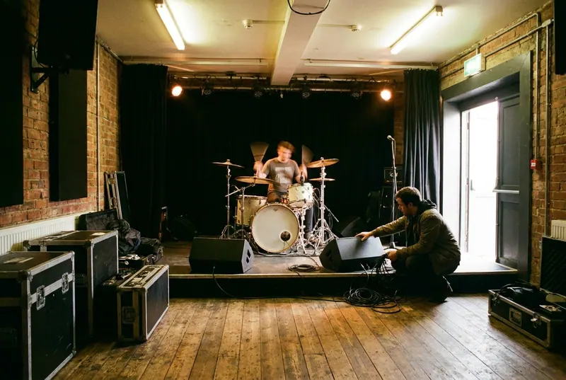 Soundcheck in an empty venue, a drummer mid-fill and an engineer at the stage edge